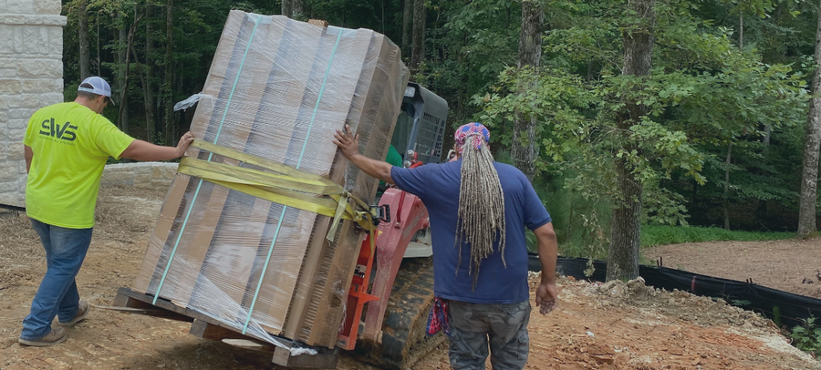 Two men moving a large wooden pallet with a forklift in an outdoor setting.